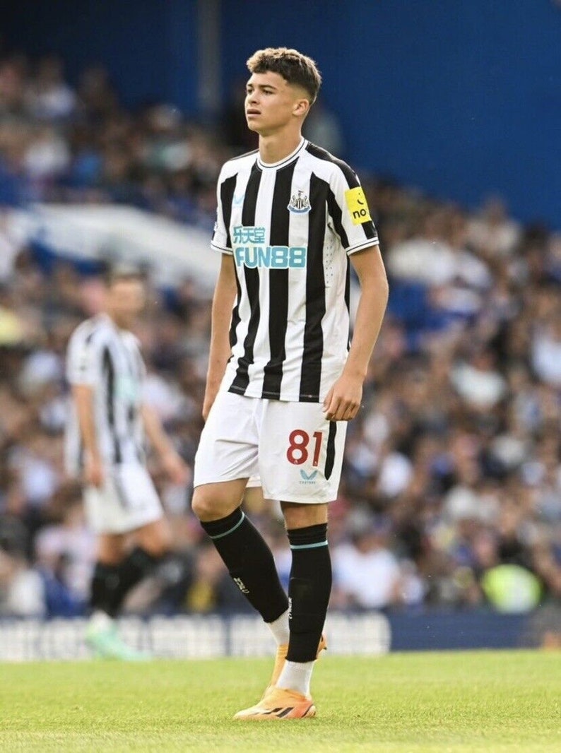 May include: A young soccer player wearing a black and white striped jersey with the number 81 on the back. The jersey has the text "FUN88" on the front. The player is wearing black socks and orange and black soccer cleats.