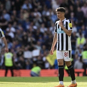 May include: A young soccer player wearing a black and white striped jersey with the number 81 on the front. The player is standing on a green field with a crowd of people in the background.