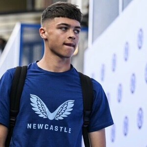 May include: A young man wearing a blue t-shirt with a white logo of wings and the word "NEWCASTLE" on it. He is wearing a black backpack and has short brown hair.