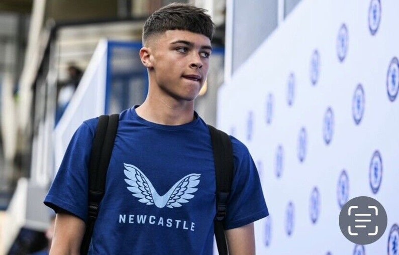 May include: A young man wearing a blue t-shirt with a white logo of wings and the word "NEWCASTLE" on it. He is wearing a black backpack and has short brown hair.