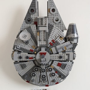 May include: A grey and red Lego Millennium Falcon spaceship with a grey and black Lego R2-D2 droid and five Lego Star Wars characters standing in front of it.