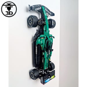 May include: A green and black Formula 1 race car model mounted vertically on a wall. The car features sponsor logos including Aramco, Boss, and JCB. The vehicle has black tyres with yellow accents and a detailed aerodynamic body design with a rear wing.