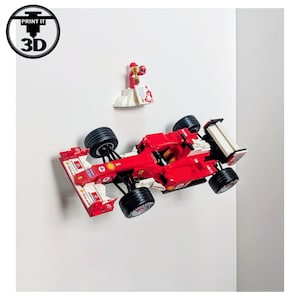 May include: A red and white toy race car with black wheels and a white rear wing. A small figurine is displayed above the car. The image has a 3D print logo in the upper left corner.