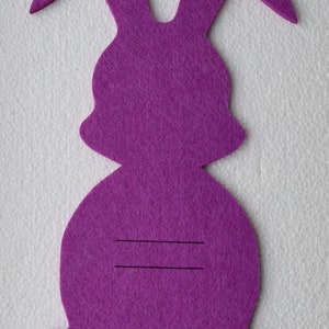 May include: Purple felt bunny shape with two lines drawn on the body.