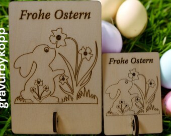 May include: Two wooden signs with a bunny rabbit and flowers, both signs say "Frohe Ostern" which is German for Happy Easter.