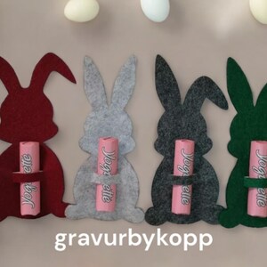 May include: Four felt Easter bunny shapes in red, gray, dark gray, and green, each holding a pink chocolate bar with the text "Yoggette" on it.