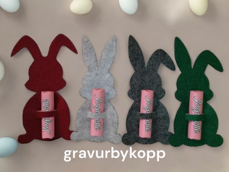 May include: Four felt Easter bunny shapes in red, gray, dark gray, and green, each holding a pink chocolate bar with the text "Yoggette" on it.