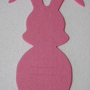 May include: Pink felt bunny rabbit cutout with two lines drawn on the body.