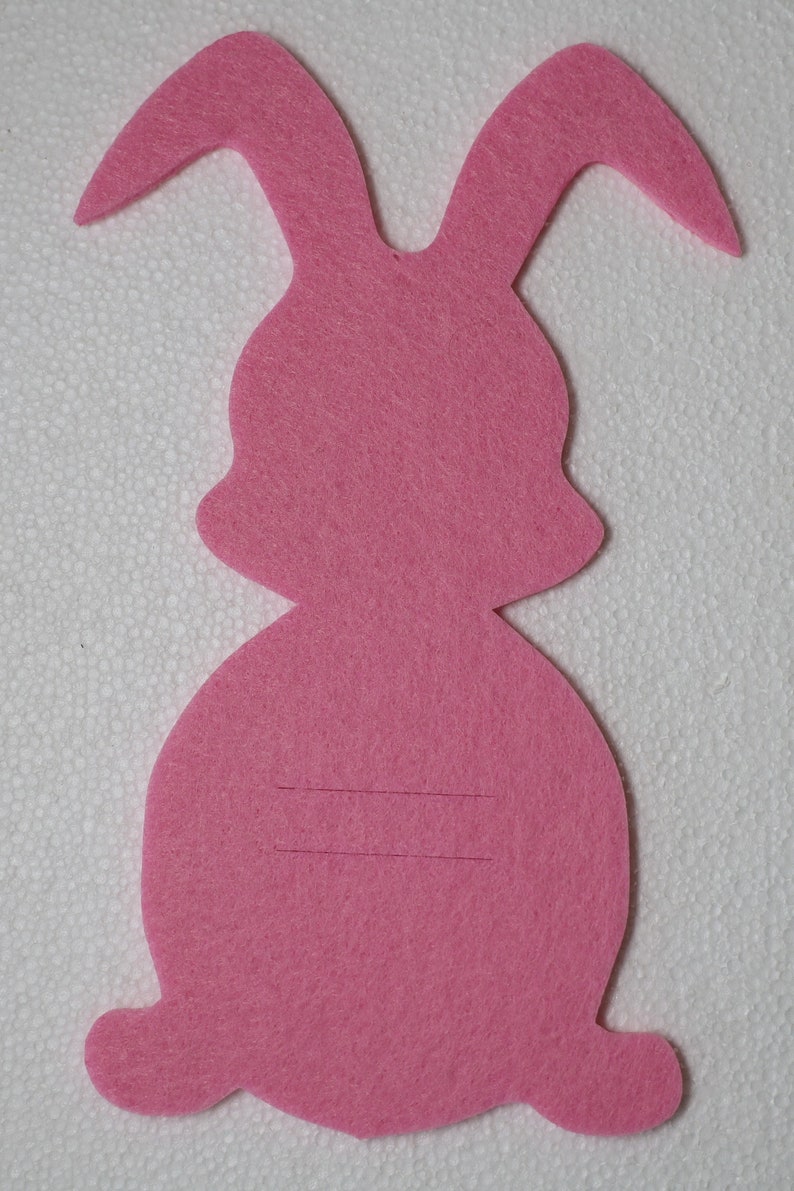 May include: Pink felt bunny rabbit cutout with two lines drawn on the body.