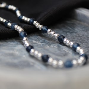 Op de afbeelding: Een zilveren en blauwe kralenketting met afwisselende zilveren en donkerblauwe kralen.