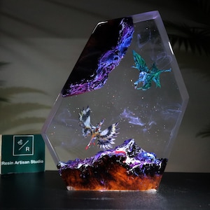 Pode incluir: Uma peça de arte em resina hexagonal transparente com uma cena de fantasia. A obra de arte inclui uma cordilheira com tons roxos e laranja, e duas criaturas míticas aladas. O fundo tem um design semelhante a uma nebulosa.