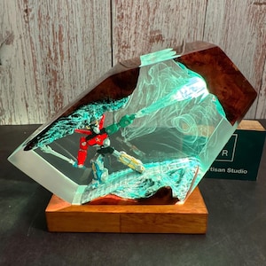 Può includere: Scultura in resina con un robot rosso, verde e giallo racchiuso in un blocco geometrico trasparente. La scultura è montata su una base di legno e ha un interno verde brillante. Altezza circa 20 cm.
