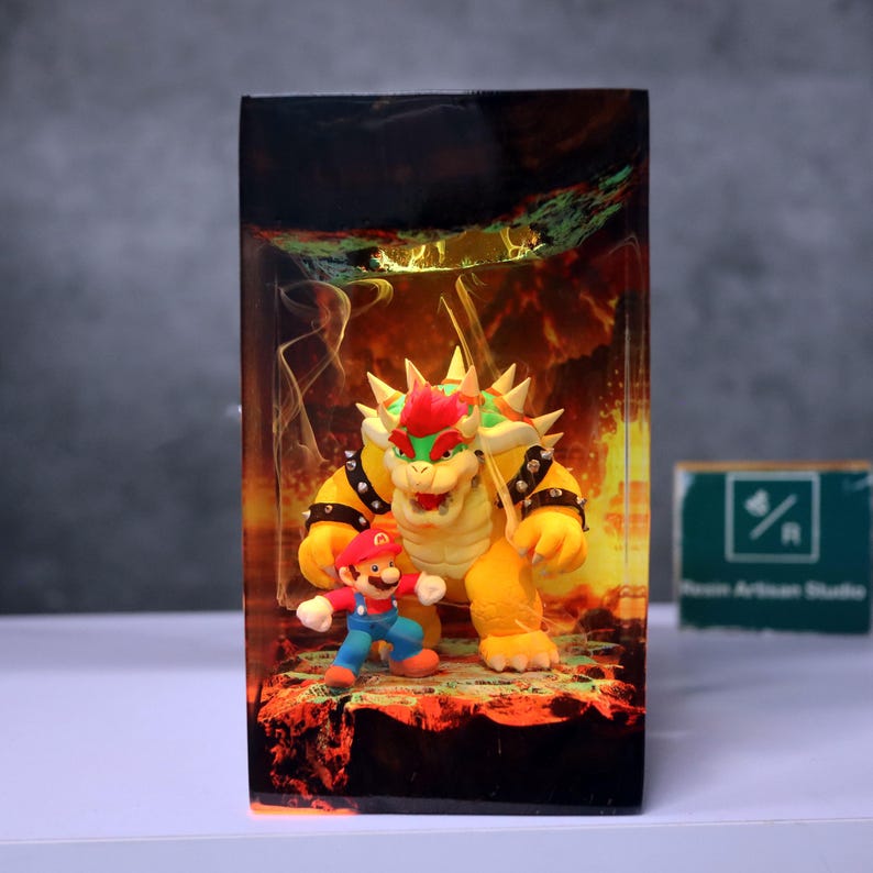 May include: A rectangular resin art piece featuring the characters Mario and Bowser from the Super Mario video game series. Bowser is yellow with a red mohawk, and Mario is in his classic red and blue outfit. The background has a fiery, lava-like design.