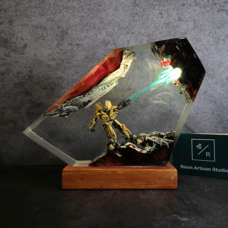 May include: A yellow robot figurine with a blue energy beam shooting out of its hand, encased in clear resin with a wooden base. The resin also contains red and white accents.