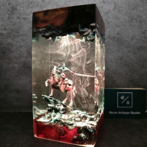 May include: A resin sculpture of a knight on horseback encased in clear resin with swirling white smoke-like patterns. The base of the sculpture is a dark red color with green and blue accents.