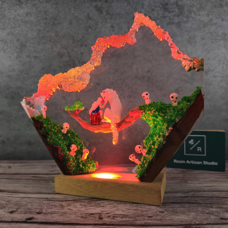 May include: A resin sculpture of a white wolf and a small creature sitting on a branch, surrounded by glowing, mushroom-like figures. The sculpture is illuminated from below, casting a warm glow on the scene. The sculpture is mounted on a wooden base and features the text "Resin Artisan Studio".