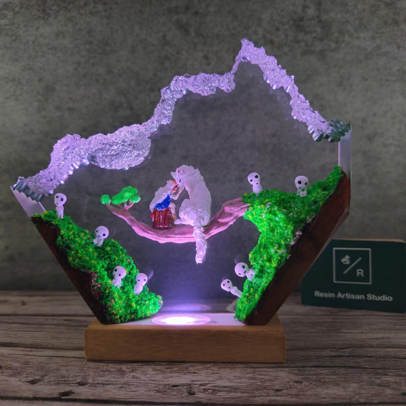 May include: A resin sculpture of a white cat and a small person sitting on a branch with a glowing light underneath. The sculpture is surrounded by small white figures and green moss. The sculpture is on a wooden base and has a sign that says "Resin Artisan Studio".