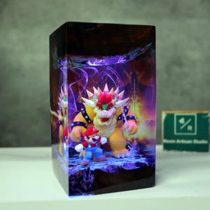 May include: A rectangular resin art piece featuring the characters Mario and Bowser from the Super Mario video game series. Bowser is yellow with red hair and spikes, and Mario is in his classic red and blue outfit. The background has a purple and orange glow.