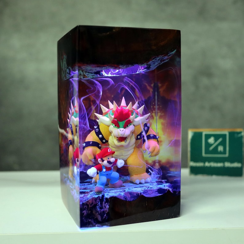 May include: A rectangular resin art piece featuring the characters Mario and Bowser from the Super Mario video game series. Bowser is yellow with red hair and spikes, and Mario is in his classic red and blue outfit. The background has a purple and orange glow.