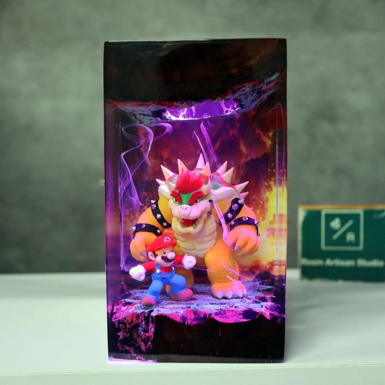May include: A rectangular resin art piece featuring the characters Mario and Bowser from the Super Mario video game series. Bowser is a large, yellow turtle-like creature with a red mohawk. Mario is in his classic red and blue outfit.