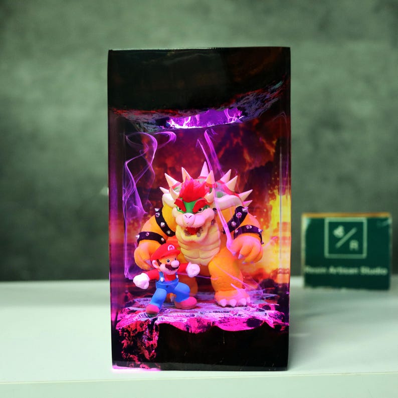May include: A rectangular resin art piece featuring Bowser and Mario figures set against a fiery background with purple and orange hues. The artwork is illuminated with internal lighting, creating a vibrant display.
