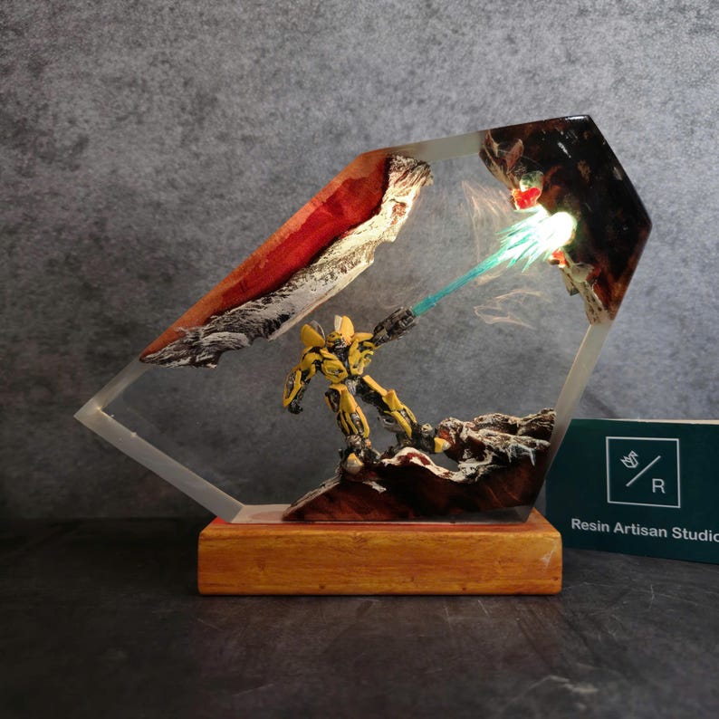 May include: A yellow robot figure with a blue energy beam shooting from its hand, encased in clear resin with a wooden base. The resin piece is shaped like a diamond and features a red and white rock formation.