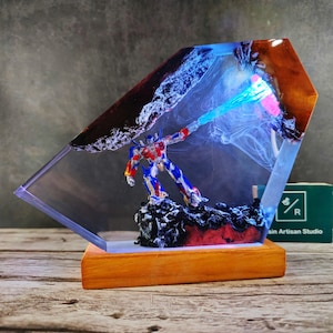 May include: A resin sculpture of a robot holding a blue energy beam, encased in a clear resin block with a wooden base. The resin block has a black and red swirl pattern.