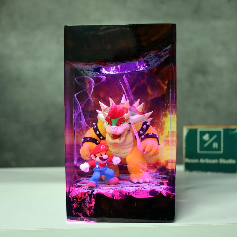 May include: A rectangular resin art piece featuring the characters Mario and Bowser from the Super Mario video game series. Bowser is a large, orange turtle-like creature with spikes, and Mario is in his classic red and blue outfit. The background has a purple and orange glow.
