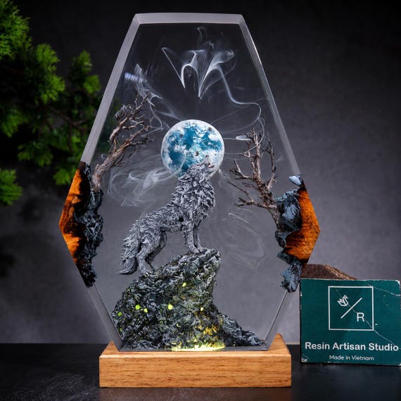 A howling wolf silhouetted against a glowing full moon, hand-cast in layered epoxy resin — it looks like a fantasy painting you can plug in.