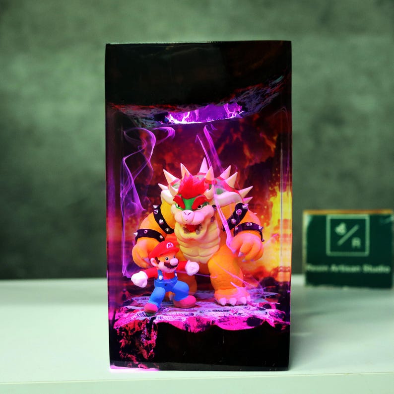 May include: A resin art piece featuring the characters Mario and Bowser from the Super Mario video game series. Bowser is a large, orange turtle-like creature with spikes, and Mario is in his classic red and blue outfit. The background has a purple and orange glow.