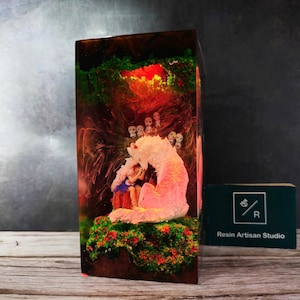 May include: A resin sculpture of a girl sitting with a pink wolf in a forest setting. The sculpture is encased in clear resin with green, red, and yellow accents. The resin block is approximately 6 inches tall.