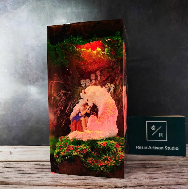 May include: A resin sculpture of a girl sitting with a pink wolf in a forest setting. The sculpture is encased in clear resin with green, red, and yellow accents. The resin block is approximately 6 inches tall.