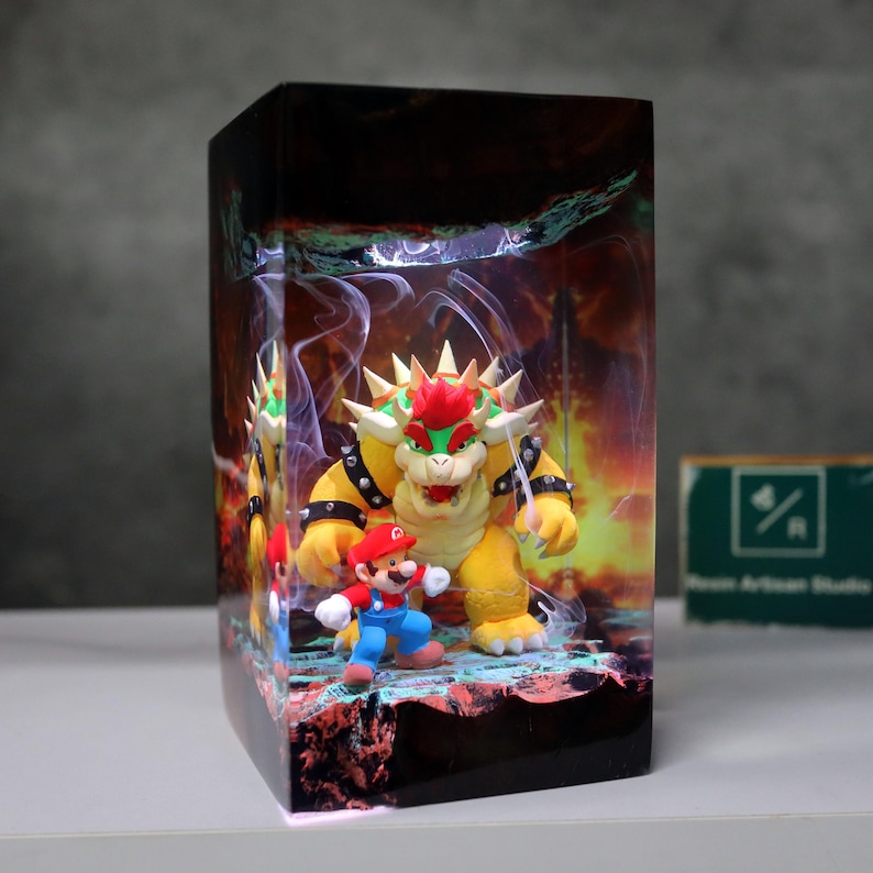 May include: A rectangular resin art piece featuring a scene with the characters Bowser and Mario from the Super Mario video game series. Bowser is yellow with a red mohawk, and Mario is in his classic red and blue outfit. The background depicts a fiery scene.