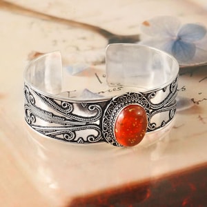 May include: Silver cuff bracelet with an ornate design and a large, oval-shaped amber stone in the center.