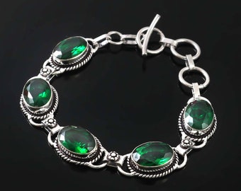 May include: A silver bracelet with a toggle clasp and five oval-shaped green gemstones. The bracelet has a delicate, ornate design.