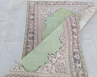 Puede incluir: Una alfombra vintage verde y rosa con un patrón floral y un borde con flecos. La alfombra está doblada por la mitad y se encuentra sobre un suelo de hormigón.