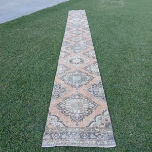 May include: A long, rectangular rug with a floral pattern in shades of pink, brown, and white. The rug is laid out on a green grassy lawn.