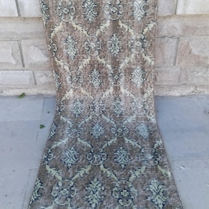 May include: A rectangular runner rug featuring a brown base color with a repeating lattice pattern in light blue and dark blue. The textile displays a symmetrical floral-inspired motif within each diamond-shaped section and has short white fringe.