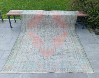 May include: A rectangular area rug featuring a central medallion design in shades of coral orange, light blue, and cream. The rug displays an intricate floral pattern with a wide decorative border, showcasing a faded, weathered appearance throughout.