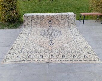 May include: A large, rectangular rug with an intricate, traditional design. The rug features a central medallion and border in shades of blue and beige. The rug is displayed outdoors on a concrete surface.