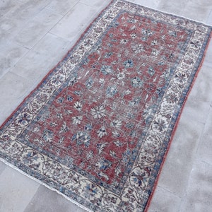 Puede incluir: Una alfombra vintage con un patrón floral en tonos rojos, azules y blancos. La alfombra tiene un borde de color crema con un diseño floral azul y rojo.