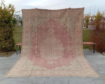 May include: A large, rectangular rug with a central medallion design in shades of red and beige. The rug features intricate floral patterns and a detailed border. The rug is displayed outdoors, showcasing its size and design.