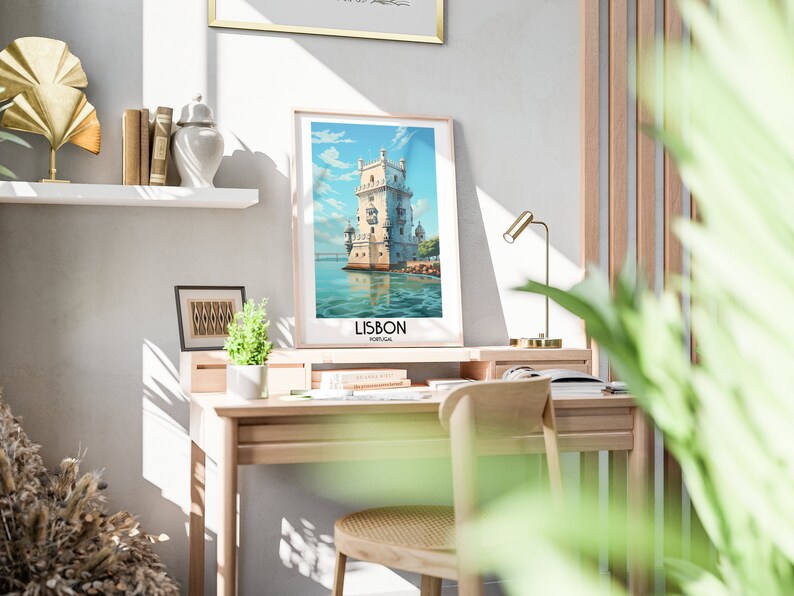 Op de afbeelding: Een ingelijste poster met een vintage reisillustratie van de Toren van Bel&eacute;m in Lissabon, Portugal. De poster hangt aan een witte muur boven een houten bureau met een stoel en een lamp.