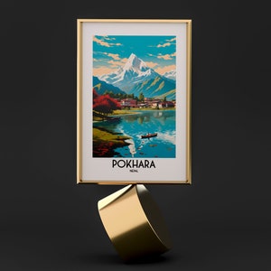 May include: A framed print of a vintage travel poster for Pokhara, Nepal. The poster features a colourful illustration of a mountain range, a lake, and a small village. The text "Pokhara, Nepal" is printed in white at the bottom of the poster.