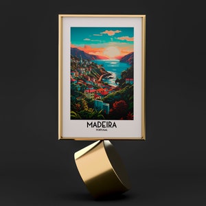 May include: A framed print of a colorful illustration of a coastal town in Madeira, Portugal. The print features a sunset over the ocean with a town built on a hillside. The text "MADEIRA PORTUGAL" is printed below the illustration.