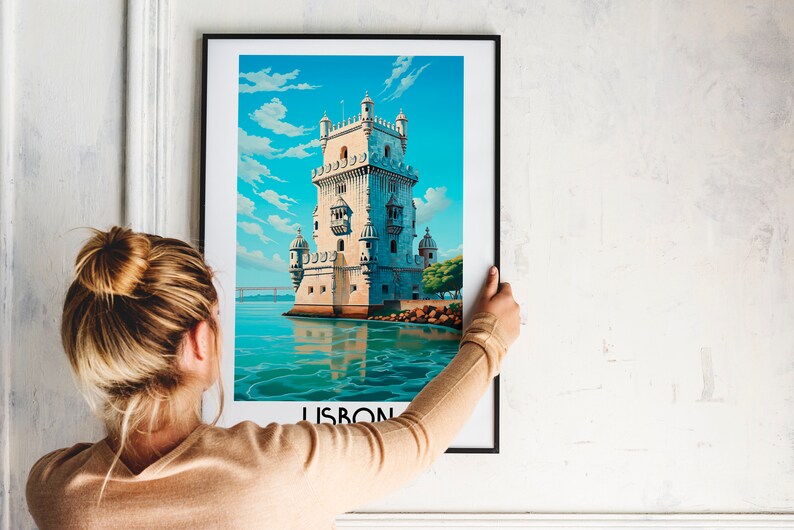 Op de afbeelding: Een ingelijste poster met een kleurrijke illustratie van een toren in het water. De poster heeft het woord "LISBON" onderaan gedrukt.