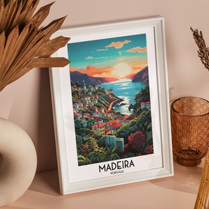 May include: A white framed print with a colorful illustration of a coastal town with a sunset in the background. The text "MADEIRA PORTUGAL" is at the bottom of the print.