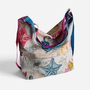May include: A hobo bag featuring a light gray background with a print of blue starfish, pink coral, seashells, and vintage-style script text. The bag includes multiple shoulder straps in solid colors of bright pink, teal, and dark blue.