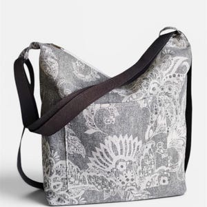 May include: Gray and white patterned shoulder bag with a black strap. The bag features a floral design and a zippered top. The strap is adjustable and the bag appears to be made of a durable fabric.