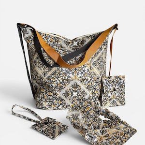 May include: A large tote bag with a black and mustard yellow strap, accompanied by a matching small pouch, a luggage tag, and a scrunchie. All items feature a repeating white, black, and gold ornate baroque-style pattern on the fabric surface.